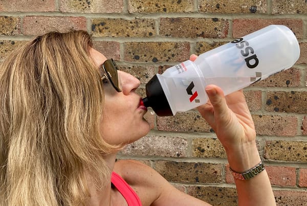 A person drinking from a water bottle in front of a brick wall.